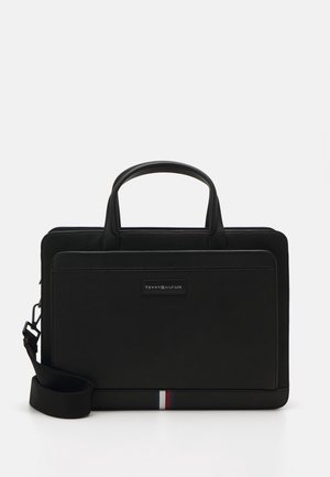 Porte-documents en cuir noir avec poignées supérieures, poche avant, bandoulière amovible et petit détail rayé rouge, blanc et bleu en bas.