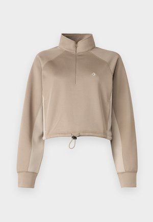 Beige cropped pullover with a high collar, quarter-zip front, and drawstring hem. Features long sleeves with contrasting side panels.