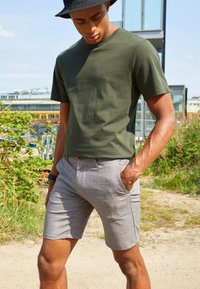 Olijfgroen katoenen t-shirt gecombineerd met lichtgrijze geruite shorts. De shorts hebben een slim fit en zijzakken, wat een casual uitstraling creëert.