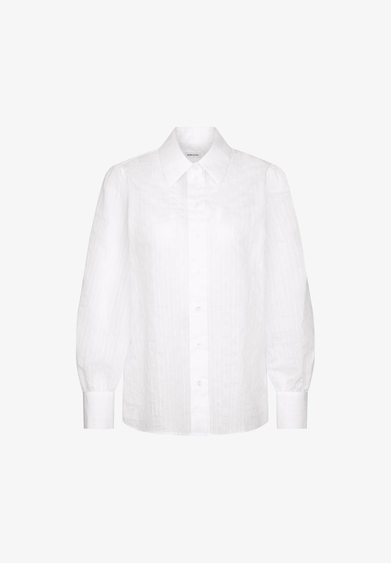 Chemise blanche à manches longues avec boutons, col pointu et manches légèrement bouffantes, présentée sur un fond blanc uni.
