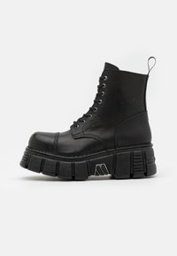Bottines en cuir noir avec une semelle épaisse et chunky, présentant un design à lacets et une languette en boucle à l'arrière. Accents de surface texturée.