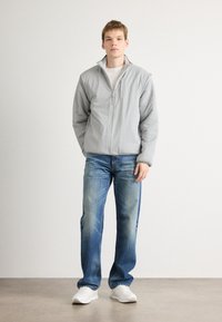 Siva zip-up jakna z ovratnikom, v kombinaciji s svetlo modrimi kavbojkami in belimi čevlji. Gladek material in udoben kroj.