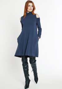 Dunkelblaues langärmliges Kleid mit hohem Kragen und schulterfreien Cutouts. Verfügt über zwei seitliche Taschen und eine lässige, ausgestellte Silhouette.