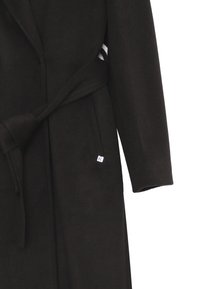 Cappotto in lana nero con una finitura testurizzata, dotato di una cintura annodata e di un piccolo etichetta bianca sul lato sinistro. Maniche lunghe e colletto a revers.