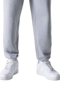 Hellgraue Jogginghose mit elastischem Bund und Seitennähten, kombiniert mit weißen Sneakern mit perforierter Spitze und Logo.