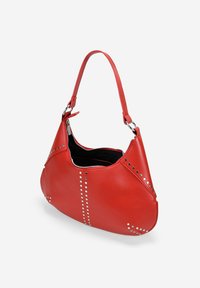 Bolso de hombro de cuero rojo con forma redondeada, que presenta tachuelas plateadas a lo largo de las costuras y un cierre de cremallera, forrado en tela negra.