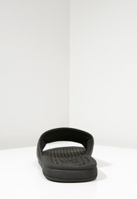 Sort slidesandal med åben tå og bag, der har en struktureret fodseng og en glat overdel, lavet af blødt og holdbart materiale.