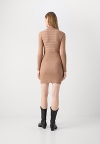 Robe en tricot couleur brun clair avec texture côtelée. Présente un design ajusté et des manches longues, associée à des bottes noires montant jusqu'aux genoux.
