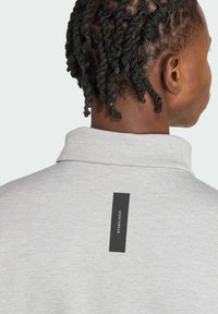 Šedá mikina s golierom vyrobená z textúrovanej látky, s čiernou nášivkou na zadnej strane s nápisom "SPORTSWEAR."