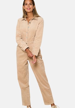 Beige corduroy jumpsuit met een kraag, knopenfront en lange mouwen. Voorzien van zijzakken en een ontspannen pasvorm. Zachte textuur.