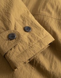 Mitra s temno sivo jakno s two gumbi, vidno šivanje in teksturno tkanino z nagubanim videzom.