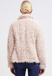 Faux furjacka i mjuk rosa, fluffig textur, bred krage och rak passform. Har lång ärm och inga synliga knäppningar.