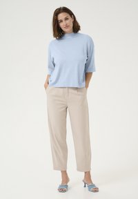 Light blue knit top with a high neckline, paired with beige tapered trousers and blue open-toe heels with frayed accents.