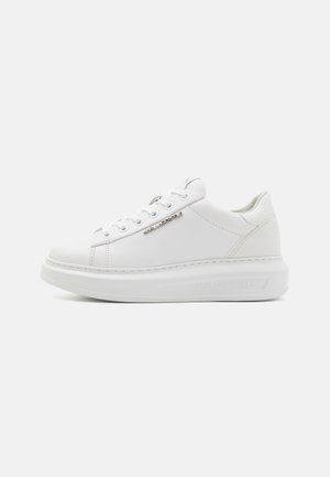 Minimalistischer weißer Sneaker mit niedrigem Schaft, dicker Sohle, weißen Schnürsenkeln und kleinem Metalllogo an der Seite.