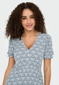 Abito blu e bianco a fantasia con scollo a V, maniche corte a sbuffo e vita arricciata. Presenta dettagli con bottoni e un tessuto leggero.