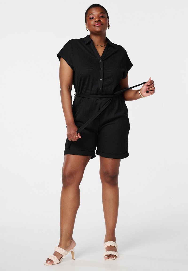 Zwarte korte mouwen jumpsuit met een knoopsluiting aan de voorkant, een terugsnoerende taille en opgerolde zoom. Draag het met lichtbeige hoge hakken sandalen.