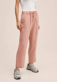 Lichtroze linnen broek met een ontspannen pasvorm, elastische tailleband, koorddetails en rechte pijpen, gecombineerd met grijze sportsneakers.