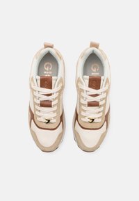 Sneakers med en beige läderöverdel, bruna mockadetaljer, vita snörning, texturerad innervaddering och en subtil logotyp på tungan.