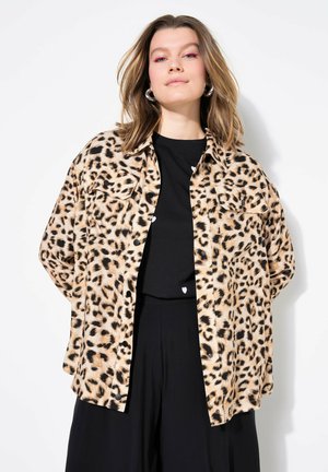 Panterprint, oversized blouse met twee voorzakken, zwarte knopen en een zachte textuur, gelaagd over een zwart shirt met een hartontwerp.