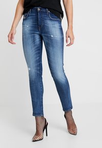 Modré džínové kalhoty se slim fit střihem, se zašlými detaily a mírně vybledlým povrchem. Spárovány s černými síťovanými podpatky.