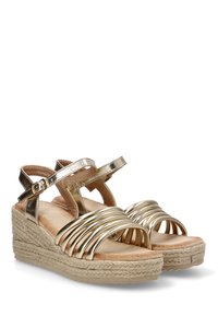 Sandalias de cuña metálica dorada con múltiples correas curvas, una plantilla de suave tono beige y una base envuelta en yute. Incluye una correa ajustable en el tobillo.