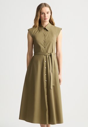 Abito verde oliva, con bottoni, a lunghezza ginocchio, dotato di colletto, maniche a campana e cintura a fiocco. Texture morbida, tessuto liscio e vestibilità sartoriale.