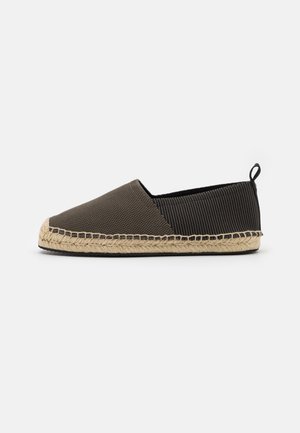 Chaussure style espadrille avec une tige en toile marron, un textile rayé noir, et une semelle en jute tressé. Dotée d'une languette pour un enfilage facile.