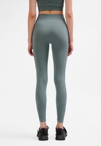Leggings a vita alta, traspiranti, in un teal opaco. Texture liscia con dettagli a costine in vita. Visibili scarpe da ginnastica nere.