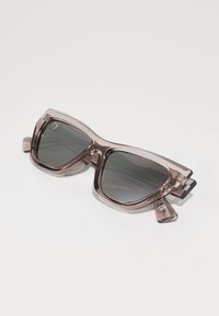Occhiali da sole con montatura sovradimensionata e angolare realizzata in plastica translucida color mauve e lenti grigio scuro. Presentano sottili dettagli metallici.
