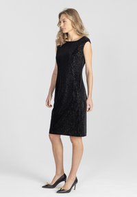 Czarna, prążkowana sukienka z dekoltem w serek i krótkimi rękawkami, o dopasowanym kroju, sięgająca tuż ponad kolano.