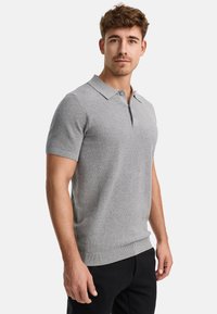Polo gris de manga corta hecho de tela de punto, con un cuello clásico y dobladillo acanalado, combinado con pantalones negros.