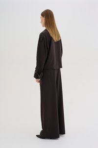 Hnědé široké kalhoty a odpovídající oversized top s vázačkami na rukávech. Hladký materiál, minimalistický design a žádné viditelné vzory.