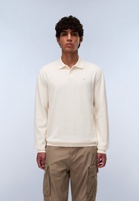 Lichtbeige poloshirt met lange mouwen, een klassieke kraag en drie knopen. Geribbelde manchetten en onderrand, gladde textuur, subtiele logodetail.