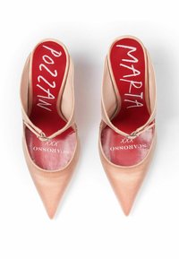 Nude satynowe mule na wysokim obcasie z ostrymi noskami, otwartym tyłem i cienkim paskiem. Wnętrze zawiera czerwone wkładki z białym tekstem.