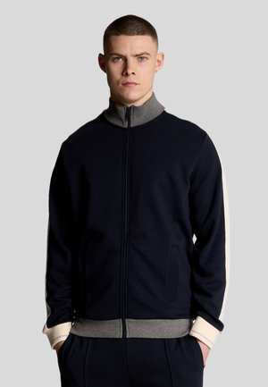 Navy zip-up jacket with light gray accents, high collar, side pockets, and contrasting stripes on sleeves. Soft material with a textured finish.