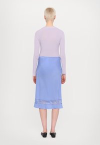 Langsleeve lavendelkleurig topje gecombineerd met een lichtblauwe rok tot de knie met een doorzichtige zoom. Model draagt zwarte ballerina's.