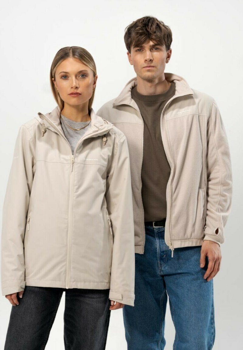 Vaaleanbeige vetoketjulla varustetut takit, joissa on huppuja, sivutaskuja ja vetoketjukiinnitykset. Naisten takin pinta on sileä, kun taas miesten takki on teksturoitu.