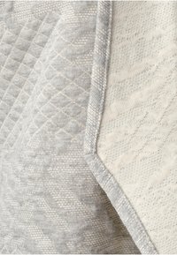 Texturerad grå och krämfärgad tyg med ett diamantquiltat mönster, med en slät yta och kontrasterande kantdetalj.