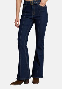 Jeans a zampa d'elefante in denim blu scuro con vita alta, cuciture a contrasto e tasche frontali. Indossati con stivali con tacco marroni.