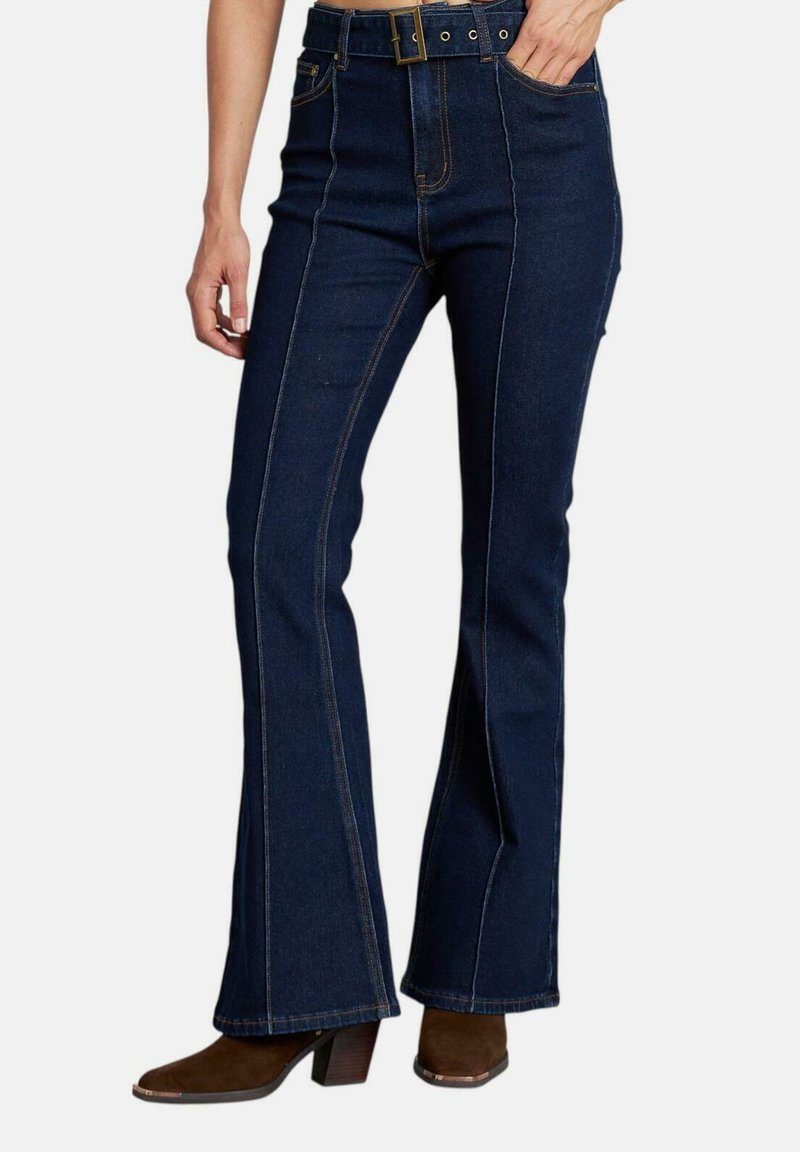 Jeans a zampa d'elefante in denim blu scuro con vita alta, cuciture a contrasto e tasche frontali. Indossati con stivali con tacco marroni.
