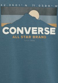 Mountain silhouette with sun behind, coordinates 42.3601°N 71.0589°W, Converse All Star Brand text on blue fabric background.