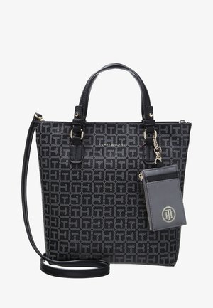 Zwarte en grijze Tommy Hilfiger draagtas met monogrampatroon, dubbele handgrepen, lange schouderriem en een bevestigd klein ritsvakje met logo.