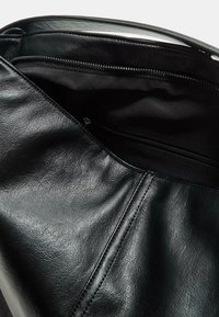 Schwarze Lederhandtasche mit texturiertem Finish. Das Innere hat ein glattes Stofffutter und eine Reißverschlusstasche zur Aufbewahrung.