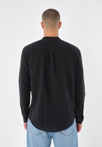 Camicia lunga nera in lino con orlo arrotondato, polsini con bottoni e una texture sottile. Design semplice, senza fantasie o accenti.