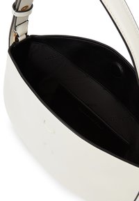 Baltā ādas plecu soma ar melnu iekšējo apdari un magnētisko aizdari, iekšpusē redzama zīmola nosaukums.