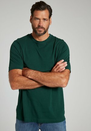 Camiseta de algodón verde oscuro con cuello redondo, mangas cortas y un corte holgado, combinada con jeans de mezclilla azul claro. La textura se ve suave.