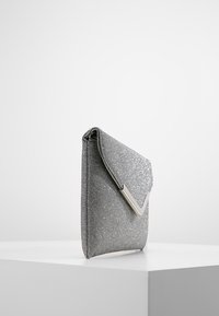 Pochette pailletée argentée avec un rabat triangulaire, une finition texturée et un accent métallique. Design simple et compact, forme rectangulaire.