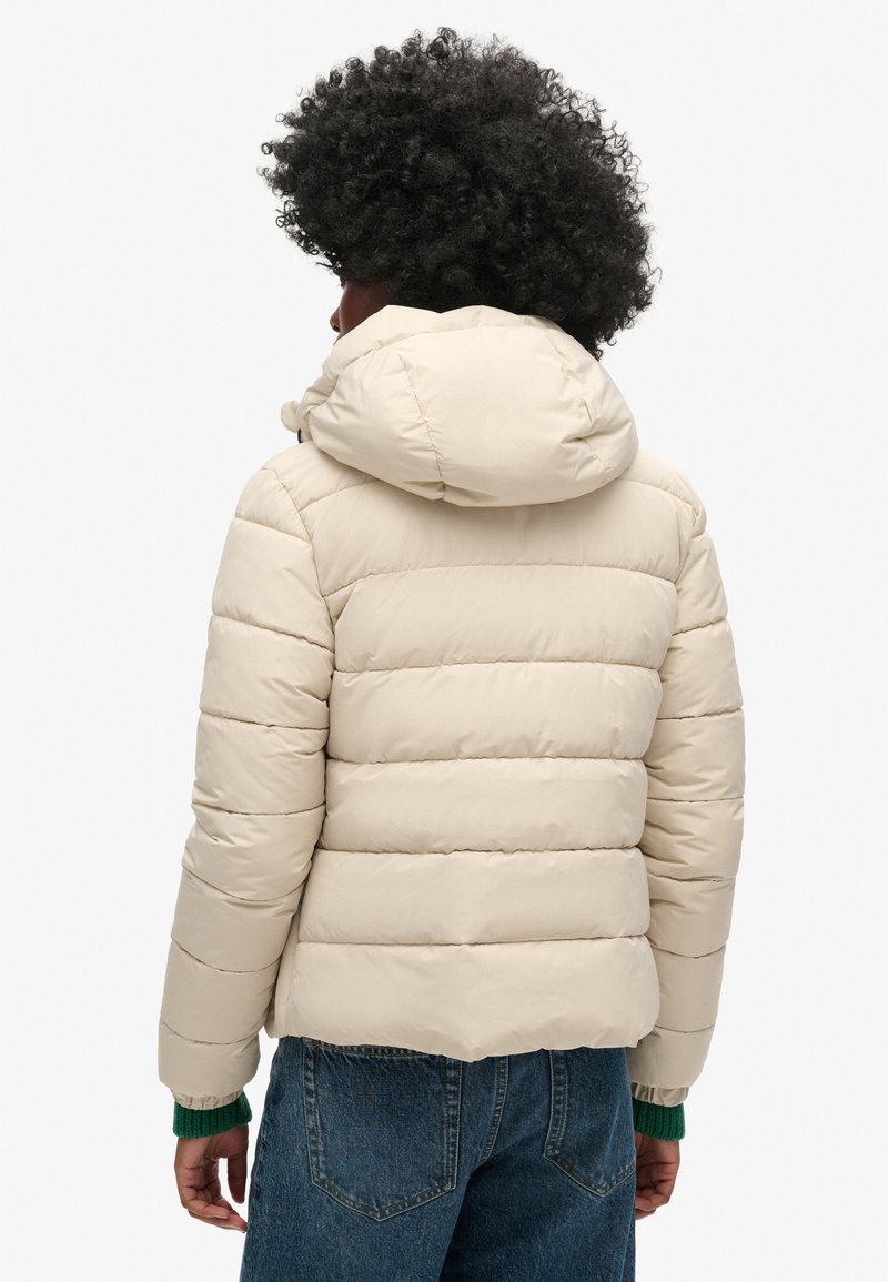 Beżowa kurtka puchowa z kapturem, z poziomym pikowaniem, elastycznymi mankietami i skróconym krojem. Gładka faktura, lekki materiał.