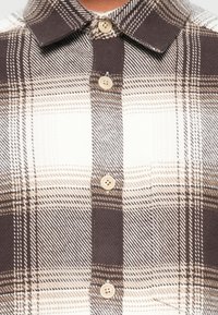Rutet skjorte i brune og kremfargede toner, med knappelukking i front, krage og distinkte ruter. Laget av et teksturert stoff.