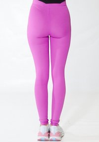 Mallas ajustadas de color rosa con textura acanalada, cinturilla alta y detalles de costura mínimos, combinadas con zapatillas deportivas blancas y rosas.